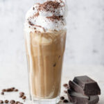 Fresh cold coffee with whipped cream and chocolate served in glass. Closeup